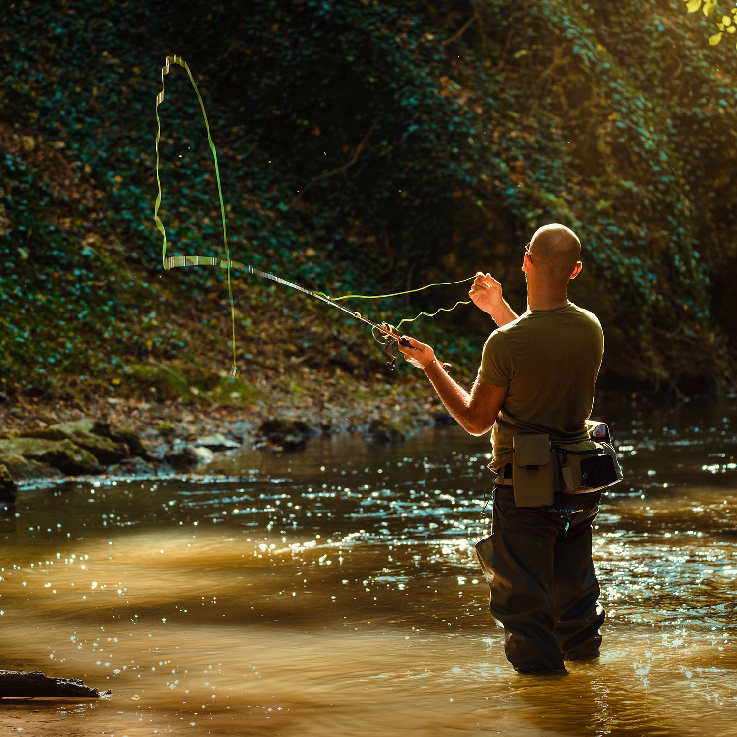 A fisherman casting his rod while almost knee deep in the Caney Creek River.