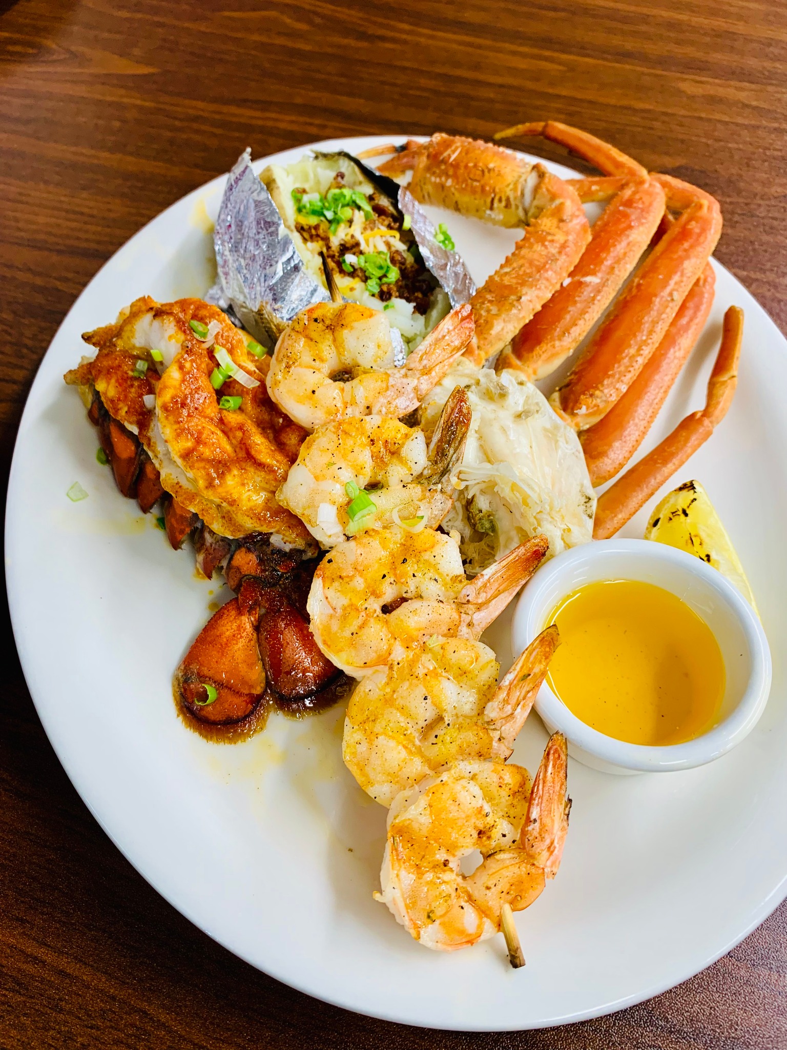 A shrimp and crab leg dish with a loaded baked potato on the side.