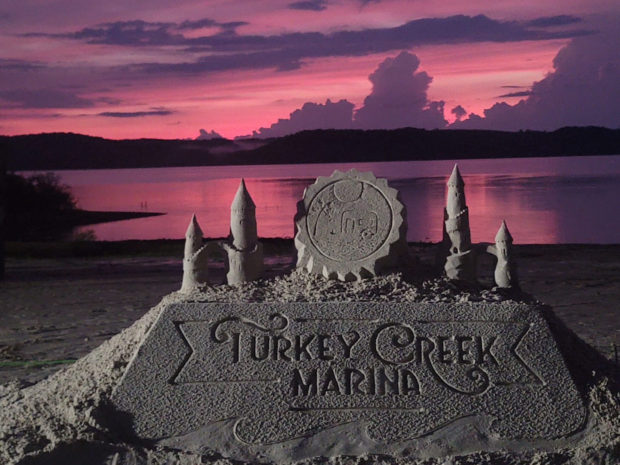 Sand castle on a lake shore with Turkey Creek Marina written on the front
