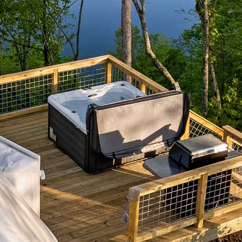 Private hot tub on a wooden deck overlooking Center Hill Lake, surrounded by trees and a stainless steel grill nearby.