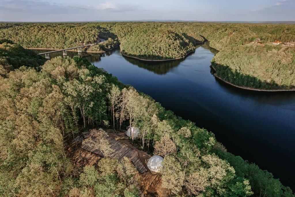 Aerial view of Center Hill Lake surrounded by forested hills, with glamping domes tucked into the trees near the shoreline—an ideal fishing getaway in Tennessee.