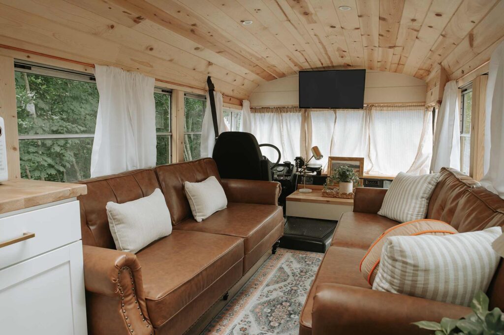Interior of Snuggle Bus skoolie rental in Tennessee with leather couches, cozy pillows, and wood-paneled ceiling, designed for comfort and Instagram appeal.